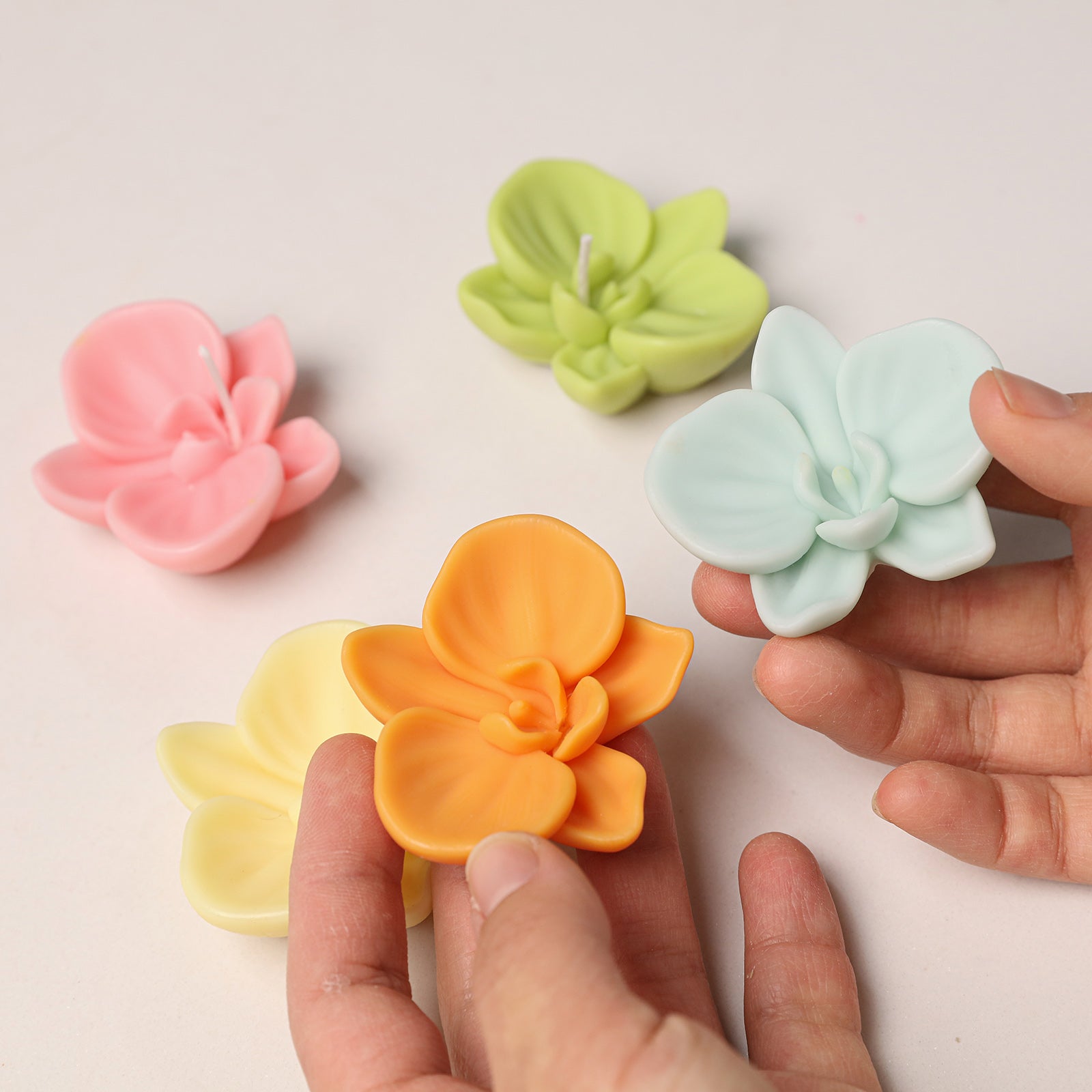 A collection of vibrant orchid wax toppers in various colors, held to show the mold's ability to create lifelike floral shapes. -Boowan Nicole
