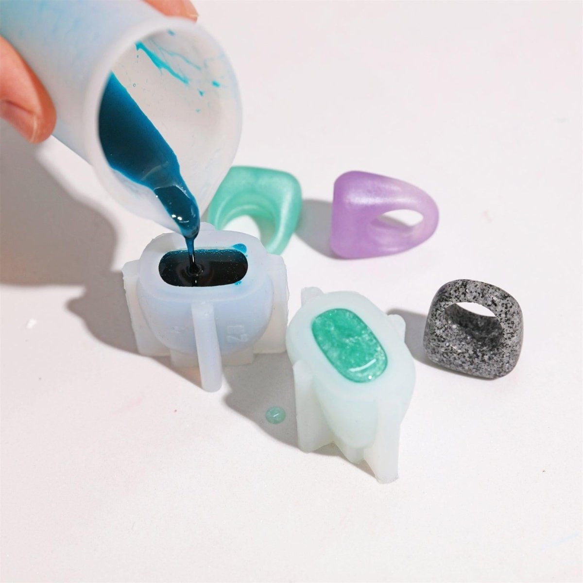 Pouring blue resin into a silicone ring mold to create handmade matte-finish rings, showcasing the resin jewelry-making process-Boowan Nicole