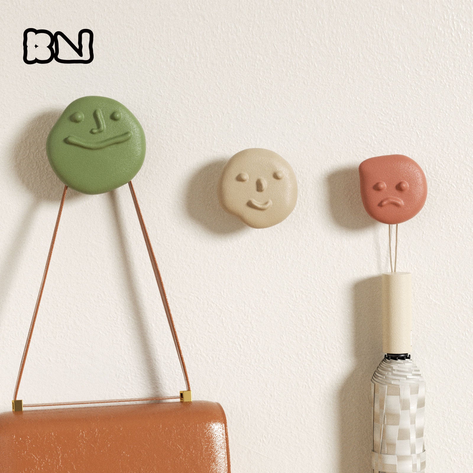 Three pebble-face wall hooks—happy, calm & pouty—in green, beige & terracotta, holding a handbag and umbrella on a white wall - Boowan Nicole