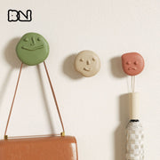 Three pebble-face wall hooks—happy, calm & pouty—in green, beige & terracotta, holding a handbag and umbrella on a white wall - Boowan Nicole