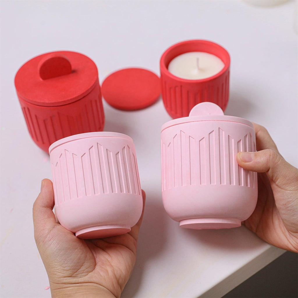 Person holding finished pink candle jars with lids, surrounded by pink jars on table - Boowan Nicole