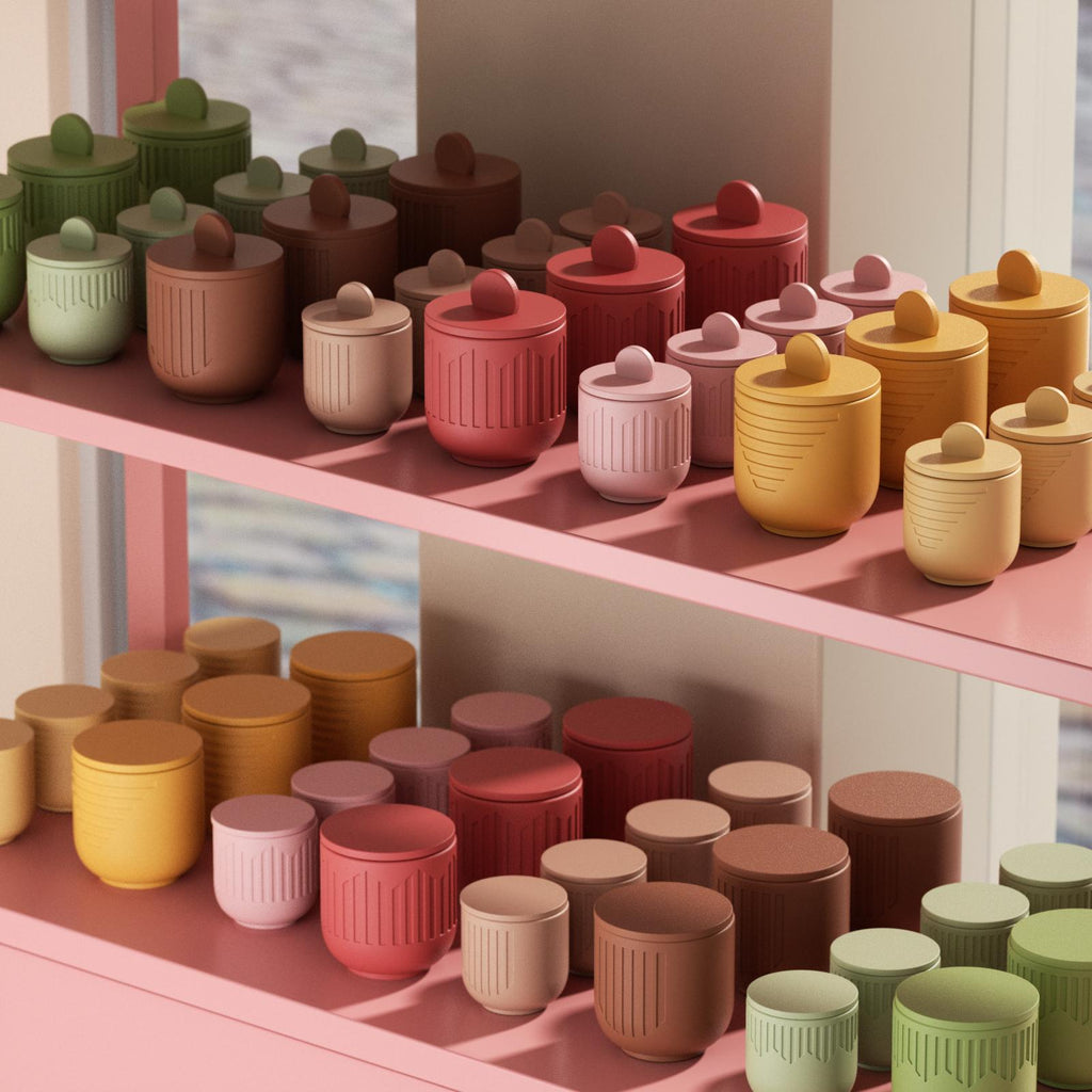Colorful ribbed candle jars with lids displayed on pink shelves, arranged by size and warm-toned colors, including red, yellow, brown, green, and pink - Boowan Nicole
