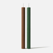 Two ribbed taper candles (brown and green) with vertical fluted texture, standing against a white background. -Boowan Nicole