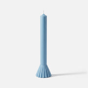 Light blue taper candle with a fluted fan-shaped base, standing against a white background. -Boowan Nicole