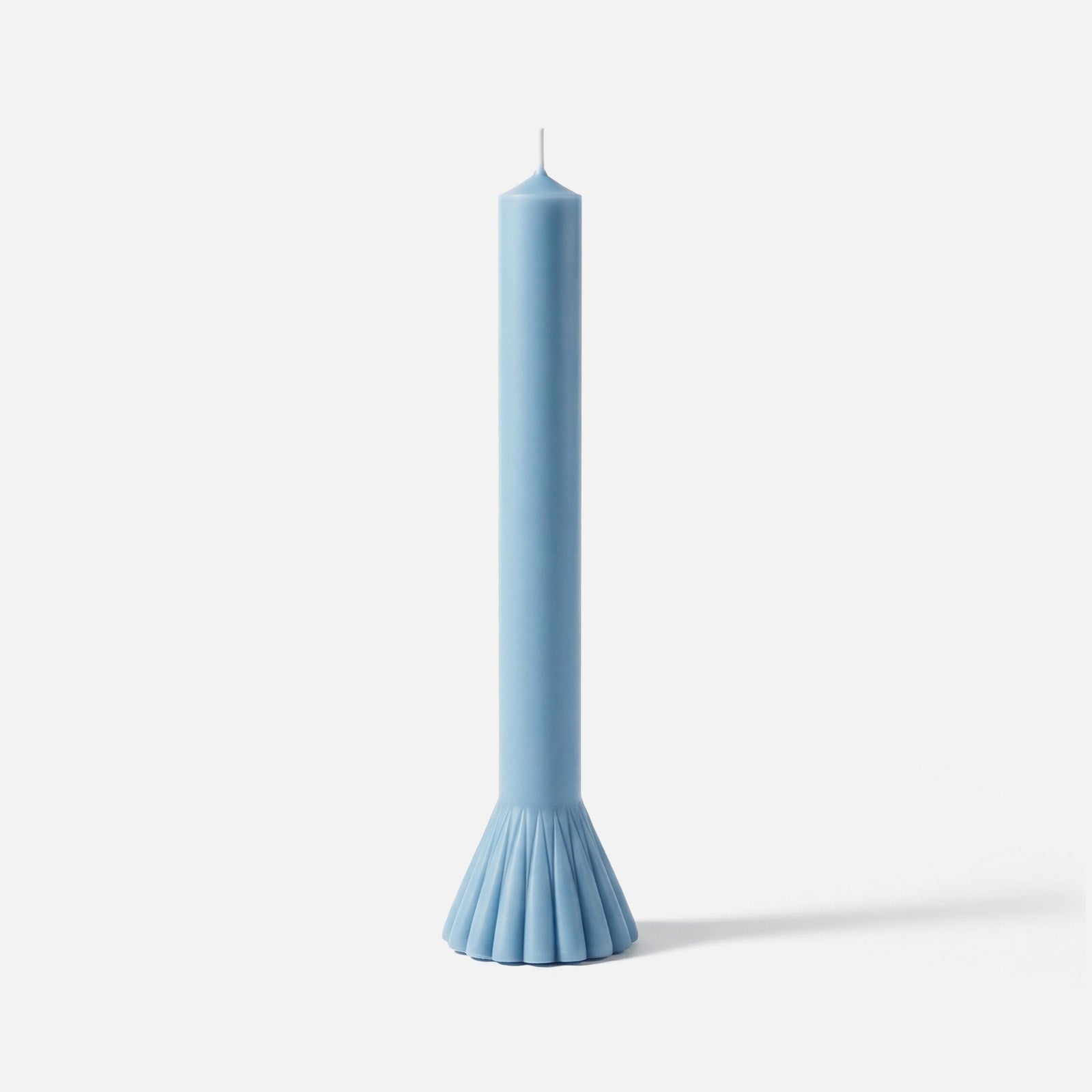 Light blue taper candle with a fluted fan-shaped base, standing against a white background. -Boowan Nicole