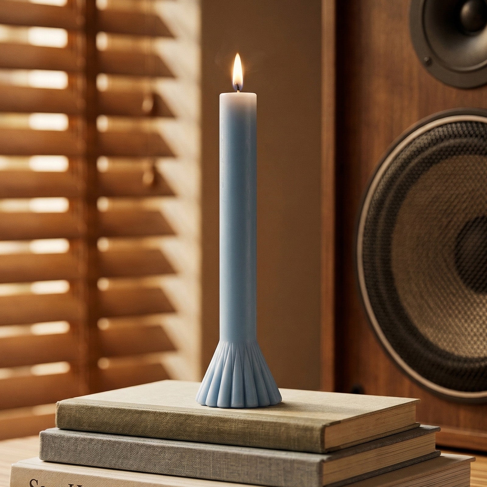 Lit light blue taper candle with a fan base, placed on stacked books with warm natural light. -Boowan Nicole
