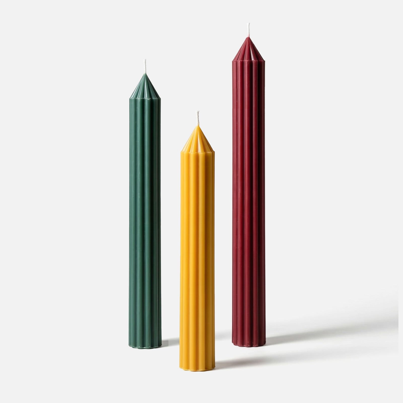 Three ribbed taper candles in deep green, mustard yellow, and burgundy red, showcasing sharp pointed tops and vertical fluted texture. -Boowan Nicole