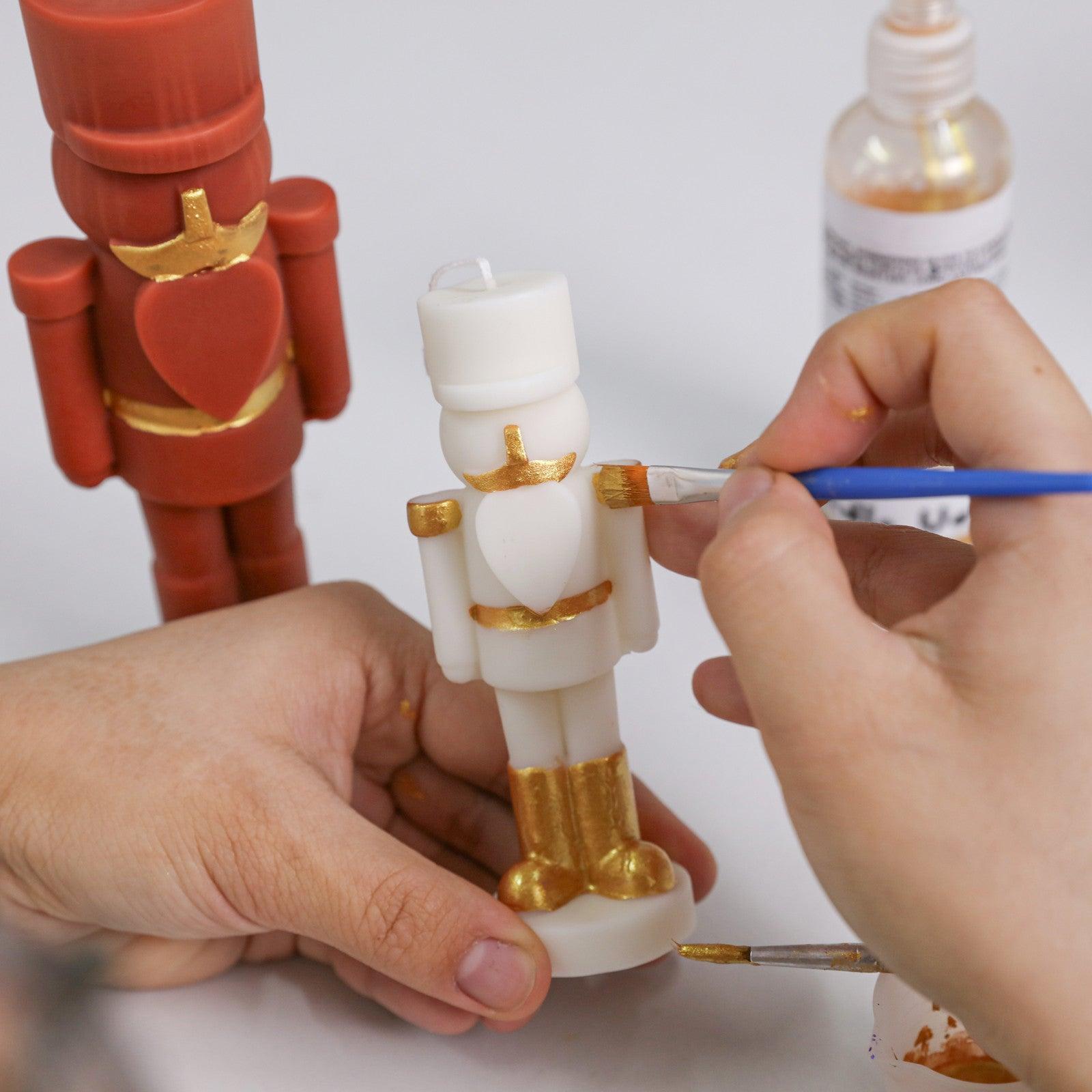 Hand-painting a white nutcracker candle with gold varnish details—perfect for festive personalization and DIY holiday crafting - Boowan Nicole