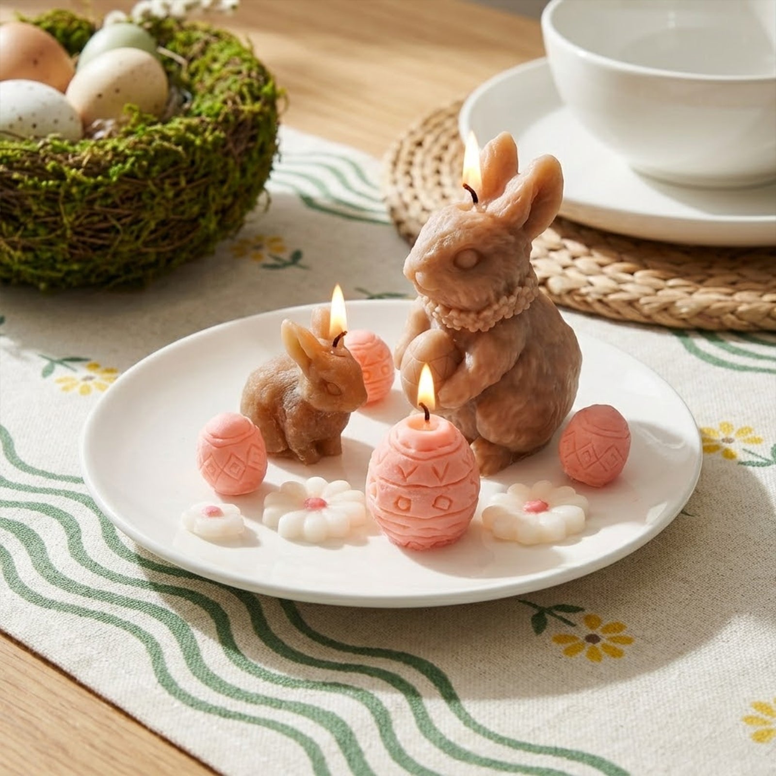 Lit brown bunny and pink egg-shaped candles on a white ceramic plate with small wax flowers, arranged as a cozy and natural Easter table centerpiece - Boowan Nicole
