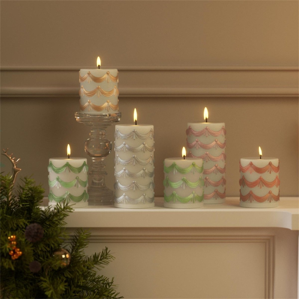 Hand-painted pillar candles with embossed garland design in soft holiday colors displayed on a mantelpiece - Boowan Nicole