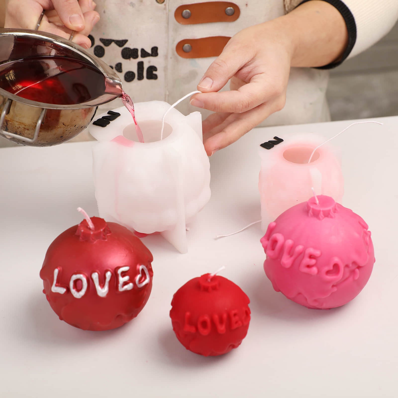 Handmade process of pouring red wax into silicone molds for LOVE themed ball candles - Boowan Nicole