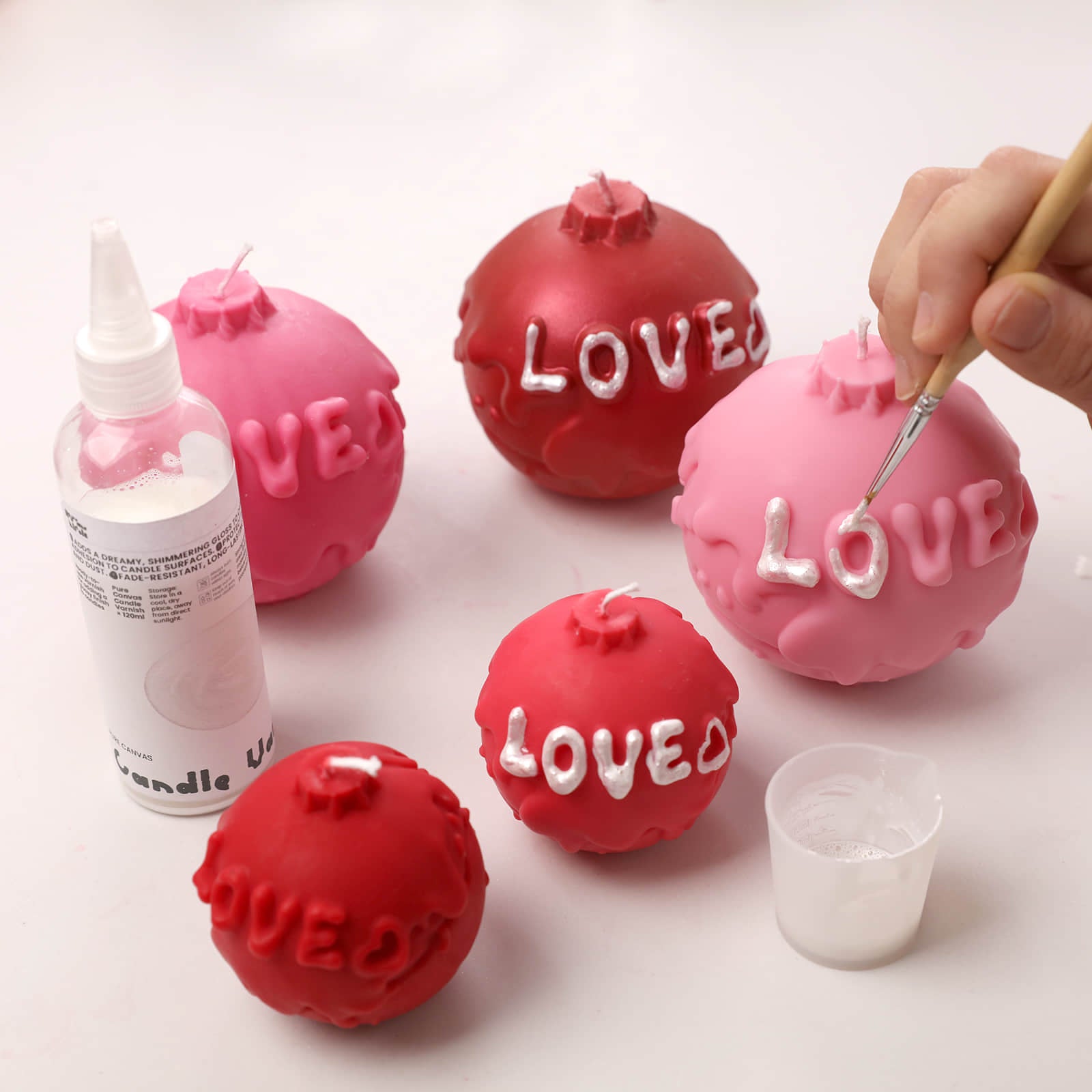 Hand-painting white "LOVE" letters on pink and red artisanal ball candles for a custom finish - Boowan Nicole