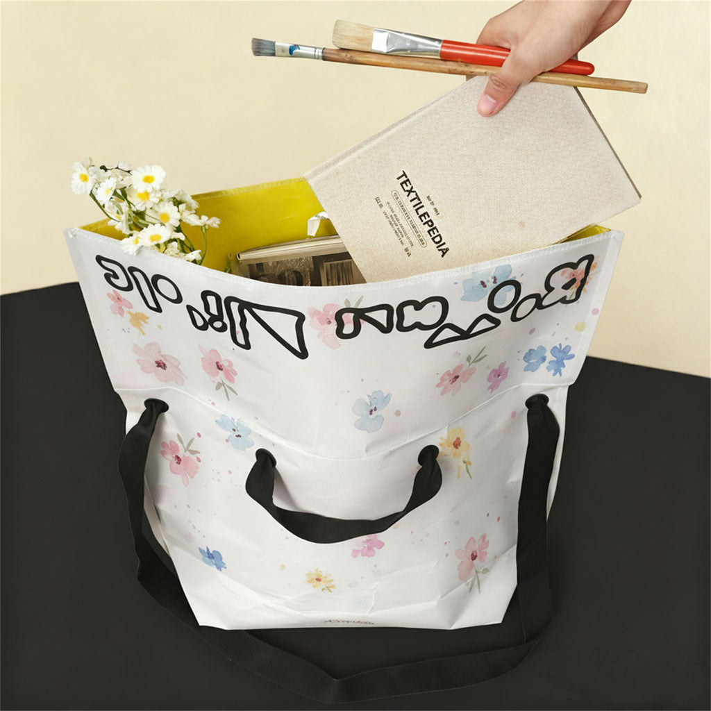 White Boowan Nicole tote bag with pastel flower doodles, black handles, and yellow lining, filled with art supplies, book, and fresh daisies - Boowan Nicole