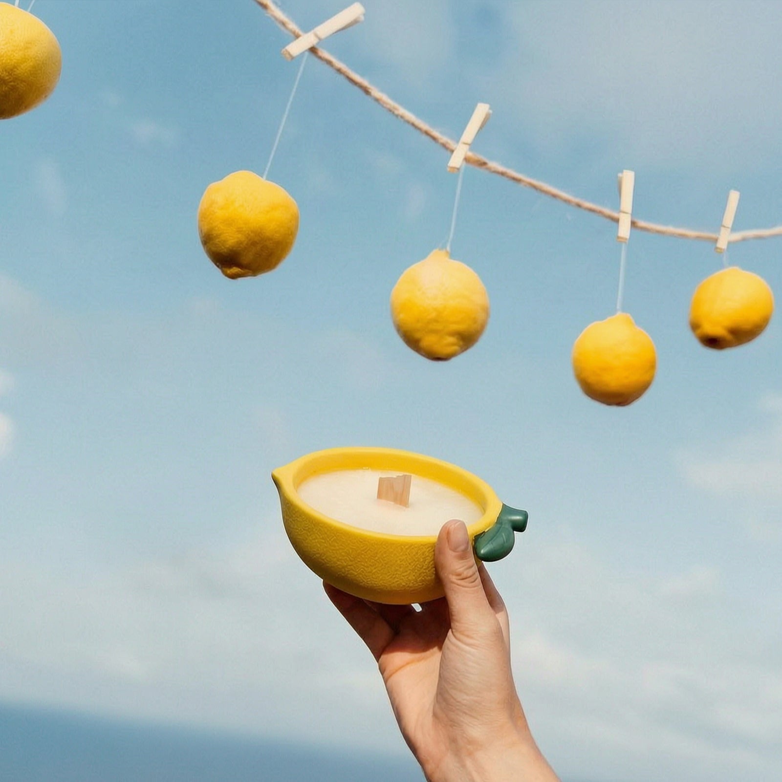 Hand Holding Handcrafted Lemon Boat Candle Against Clear Blue Sky - Boowan Nicole