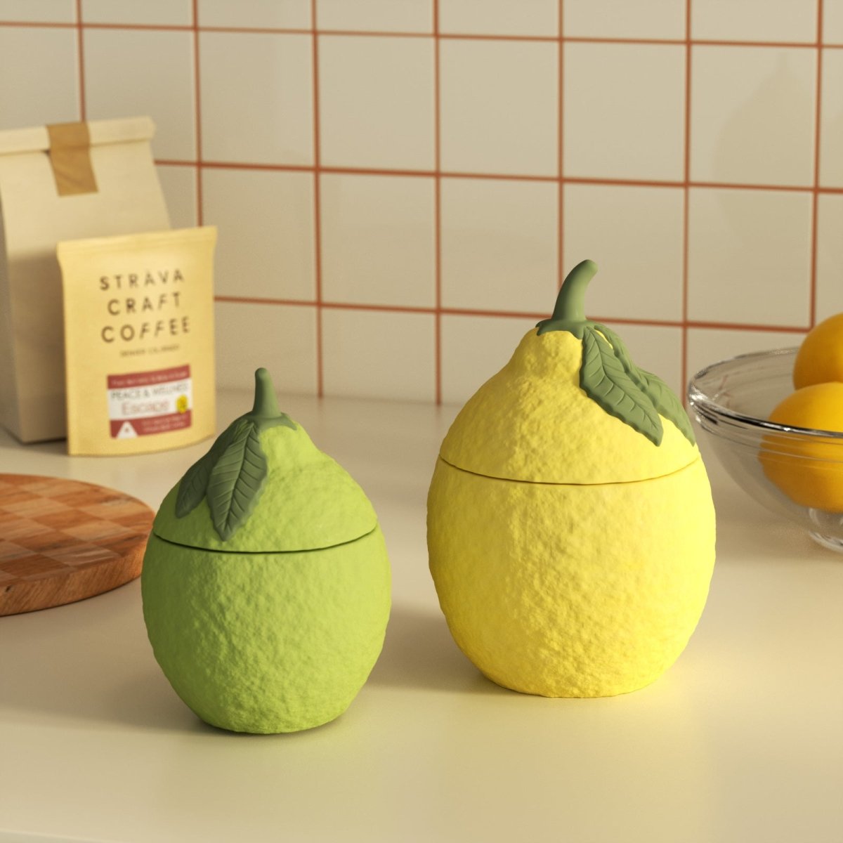 Two lemon-shaped candle jars with leaf lids—one green, one yellow—on a kitchen countertop - Boowan Nicole
