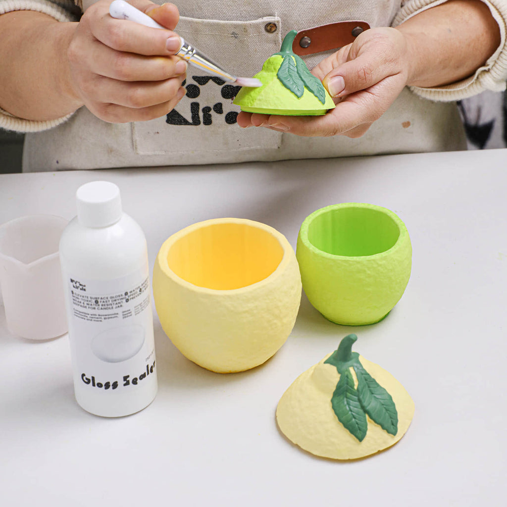 Applying a gloss sealer to the lid of a lemon-shaped candle jar - Boowan Nicole