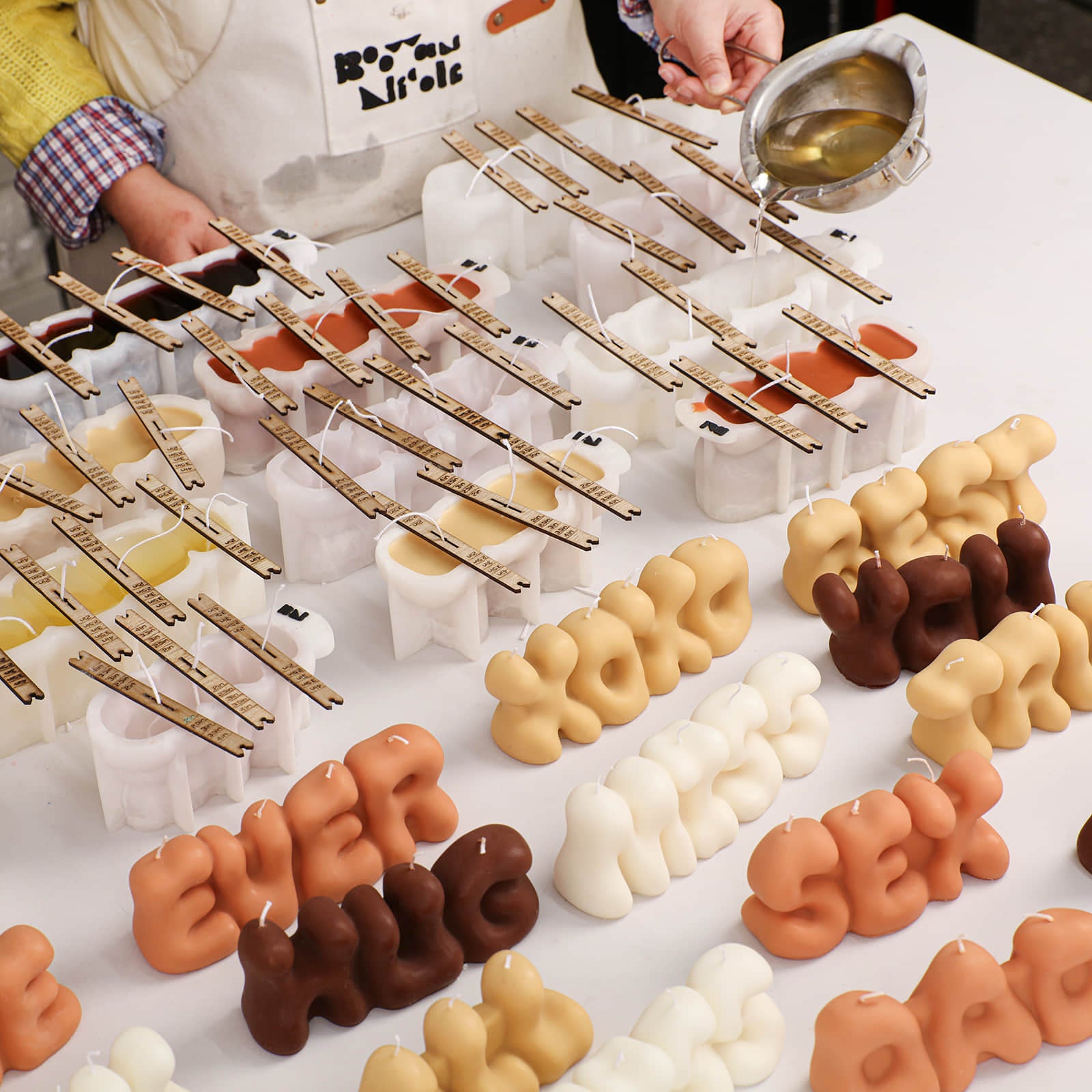 Artisan batch production in a candle studio: hand-pouring the Love Letters Candle collection in various colors - Boowan Nicole