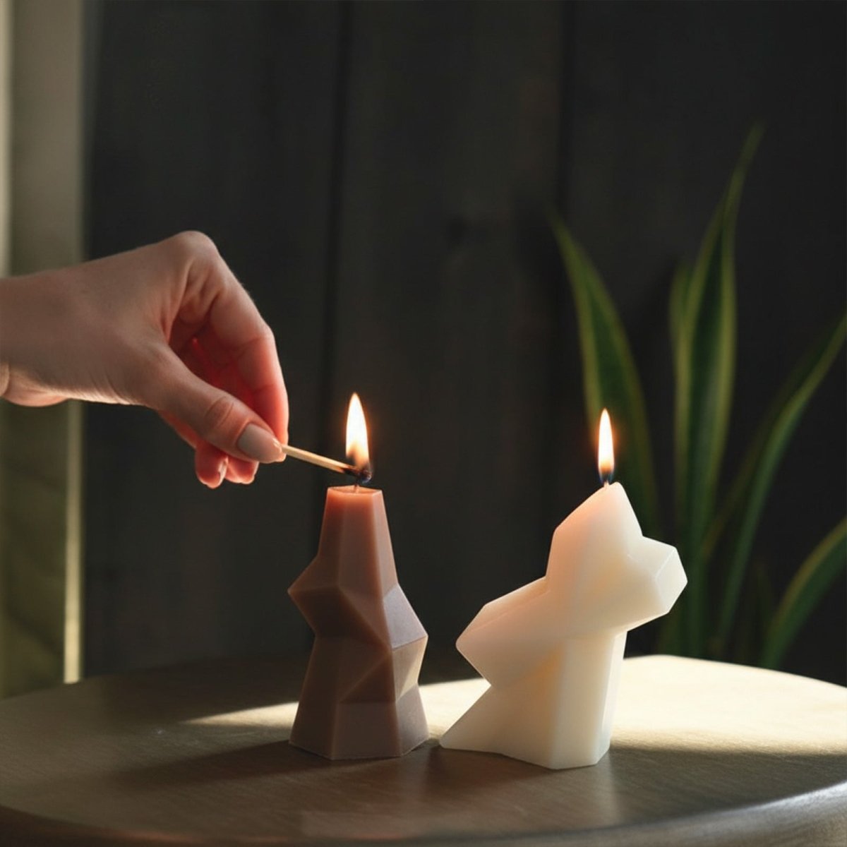 Hand lighting a faceted geometric pillar candle next to a white sculptural candle - Boowan Nicole