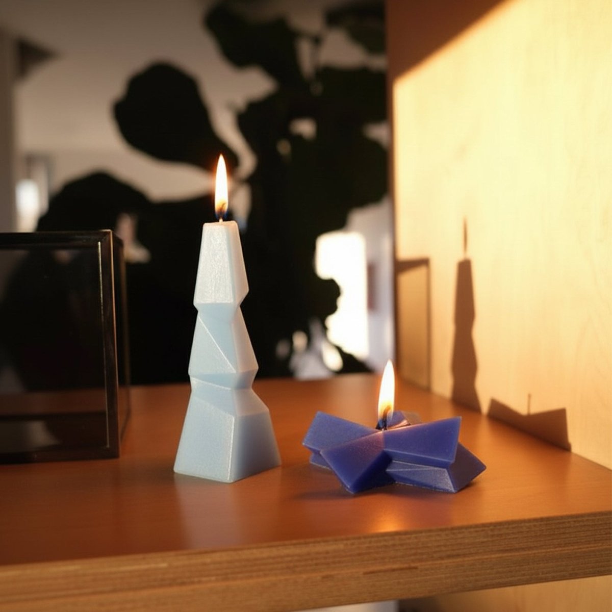 Tall light blue geometric pillar candle and low blue abstract candle burning on a wooden shelf - Boowan Nicole