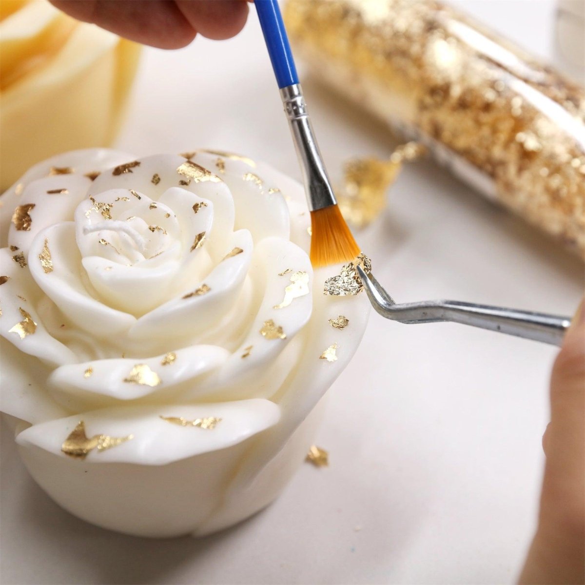 Hand-applying gold leaf on white candles using tweezers and brush - Boowan Nicole