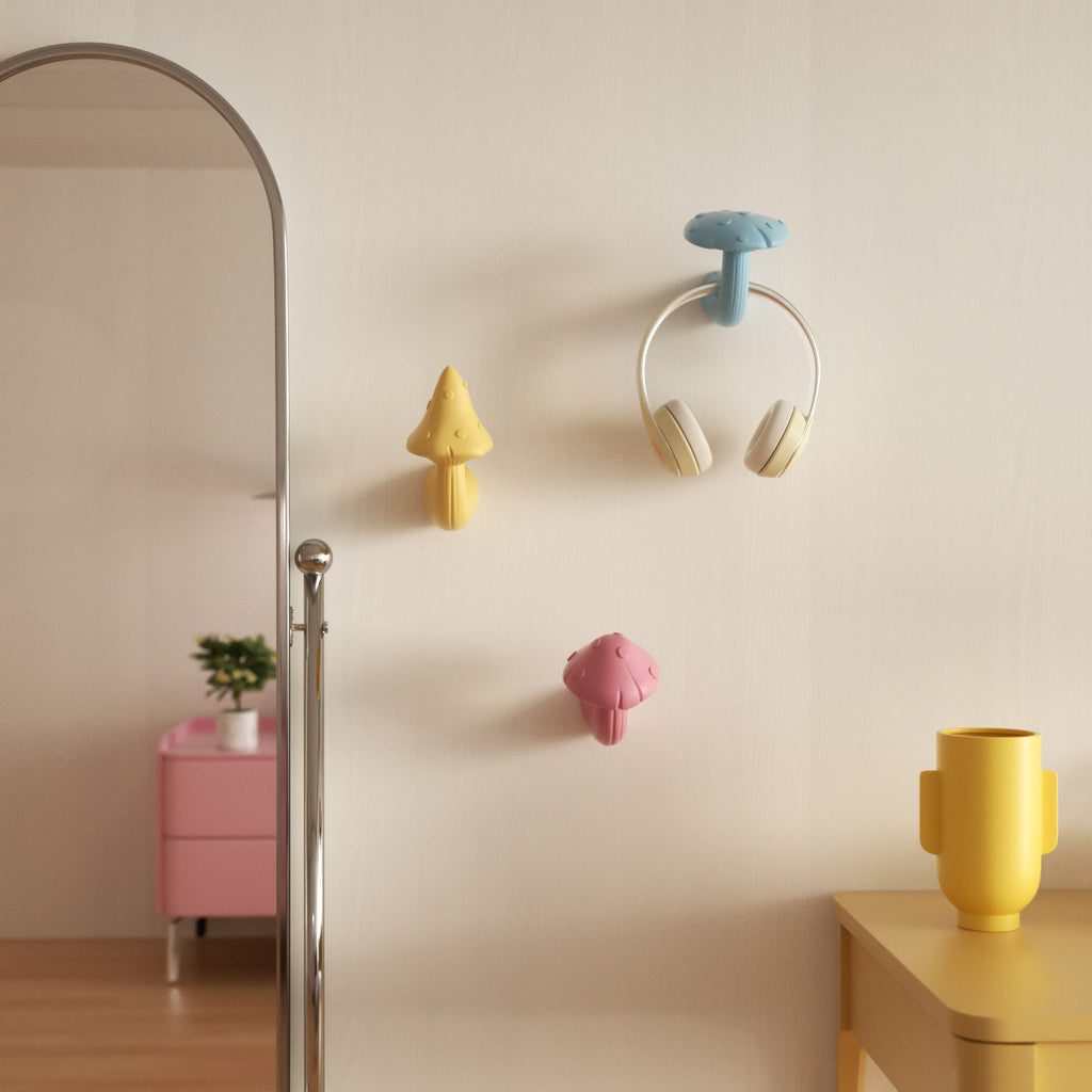 Pastel mushroom wall hooks—blue, yellow, and pink—mounted on a light wall; the blue hook holds a pair of headphones - Boowan Nicole