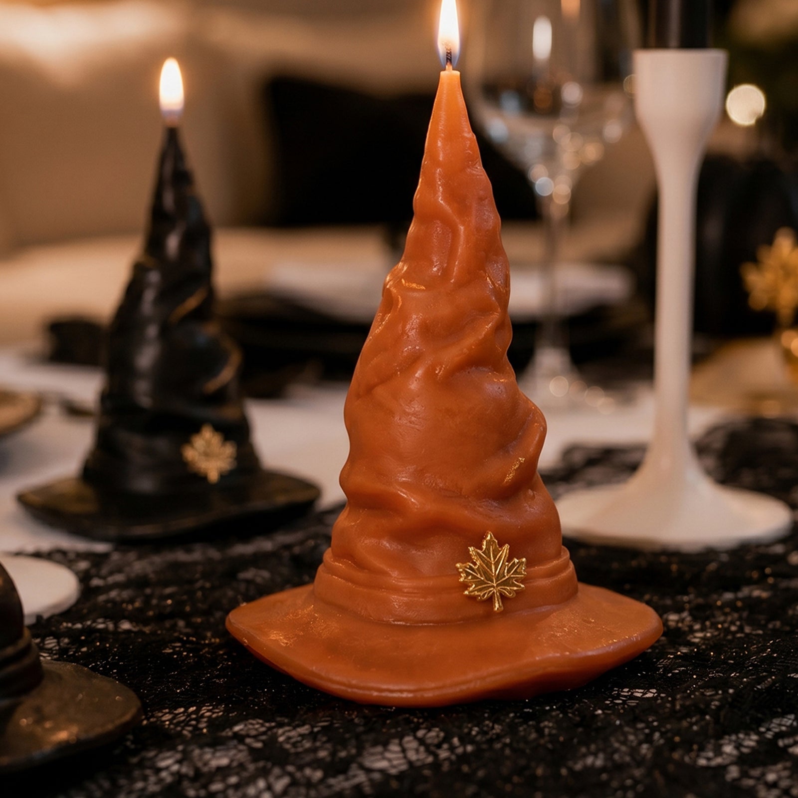 Lit orange & black mystic wizard hat pillar candles placed on black lace tablecloth Halloween dining table styling - Boowan Nicole