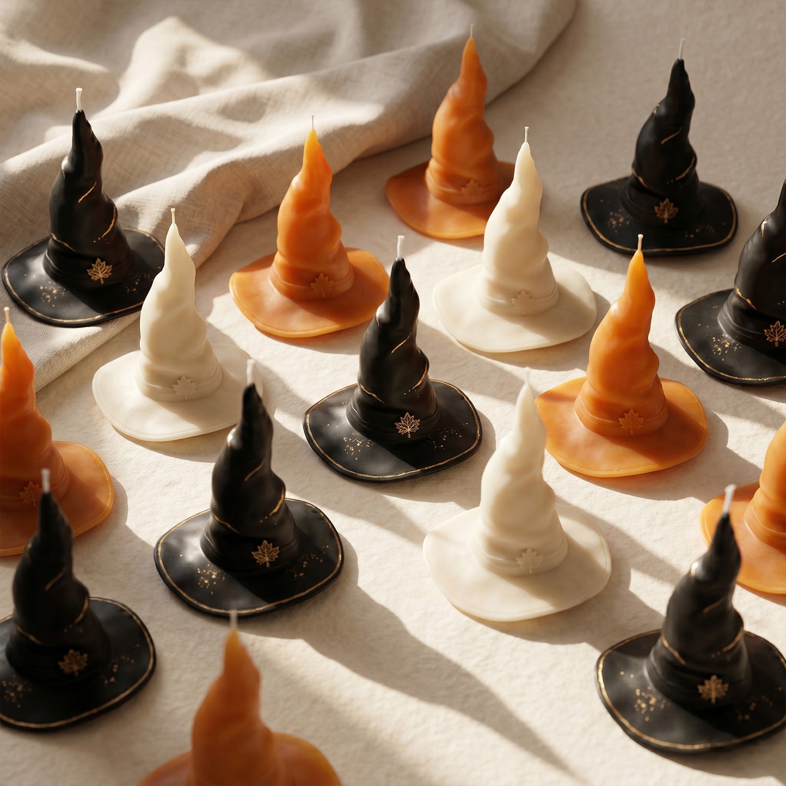 Full assortment black, cream, orange mystic wizard hat pillar candles laid flat on soft linen fabric seasonal product group shot - Boowan Nicole