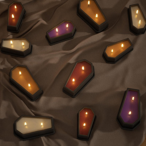 Lit coffin-shaped candles with colorful wax fills displayed on brown fabric - Boowan Nicole