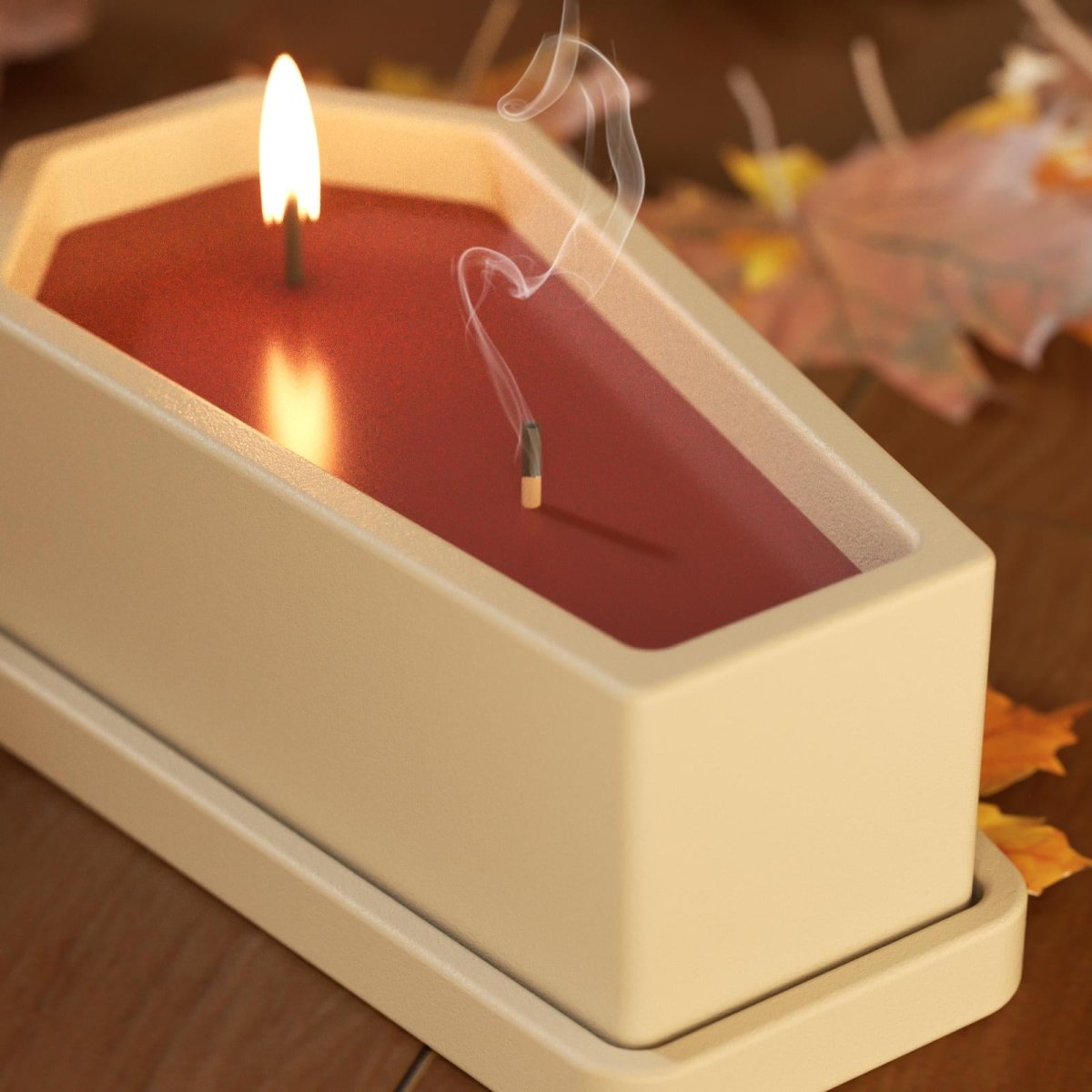 Close-up of a coffin-shaped candle with red wax and burning wick, surrounded by autumn leaves - Boowan Nicole