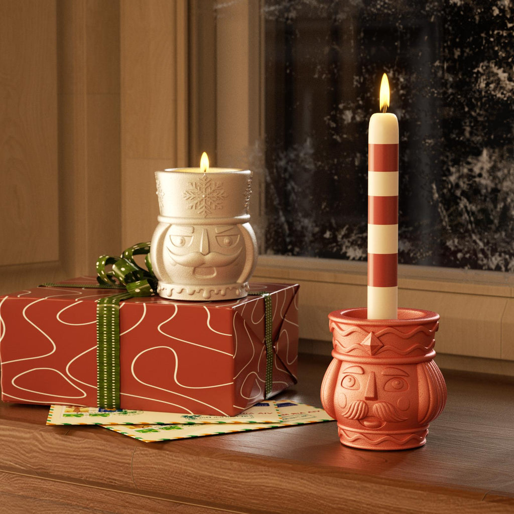 Christmas nutcracker candle holders with lit taper and tea light candles by a snowy window.