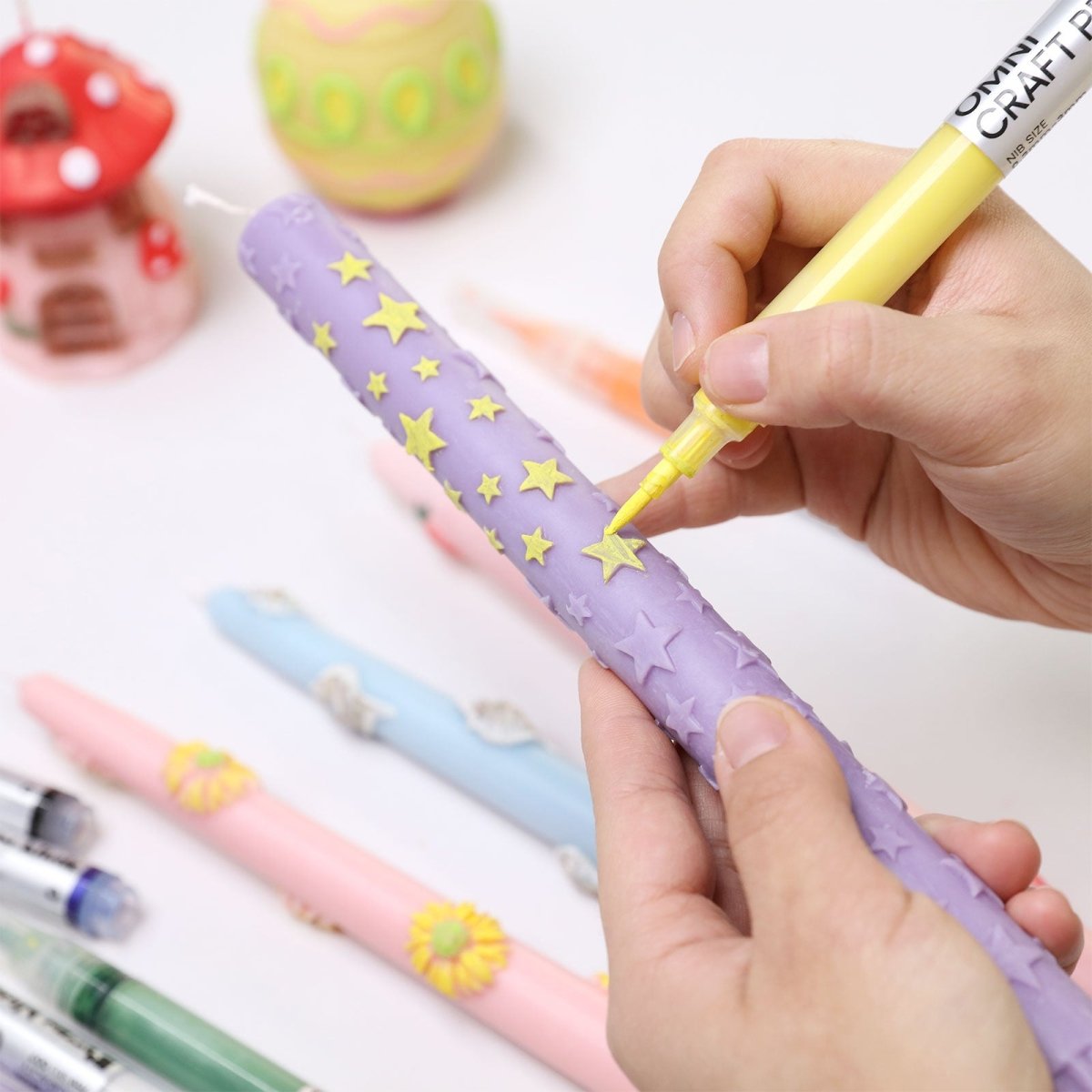 Hand decorating a lavender taper candle with yellow stars using an Omni Craft Pen refillable acrylic paint pen - Boowan Nicole
