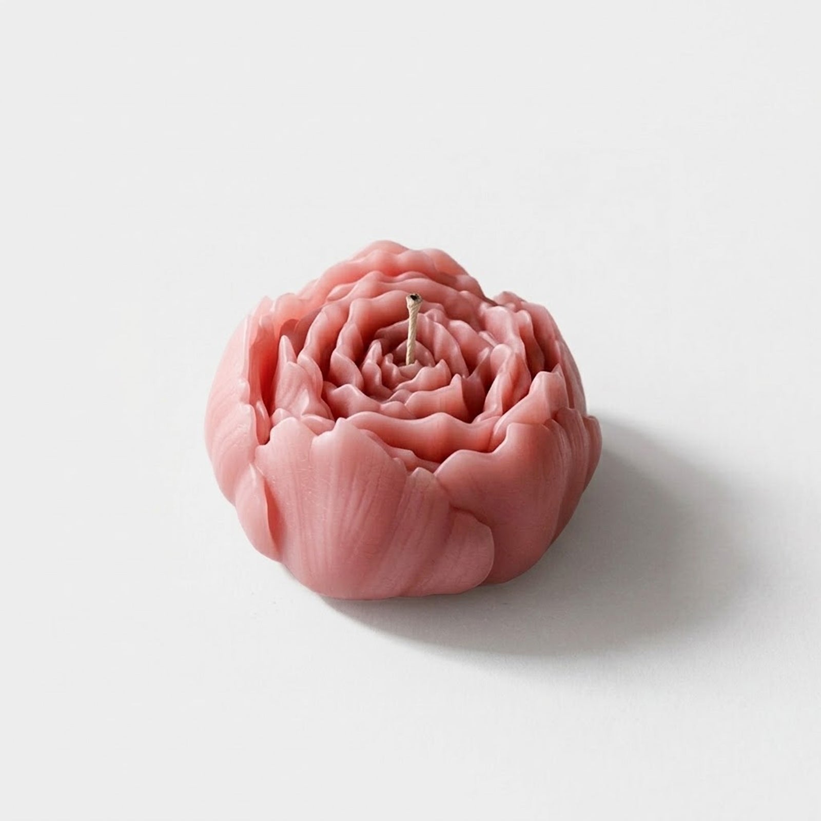 A lifelike pink peony-shaped candle with detailed layered petals, centered wick, on a white background. -Boowan Nicole