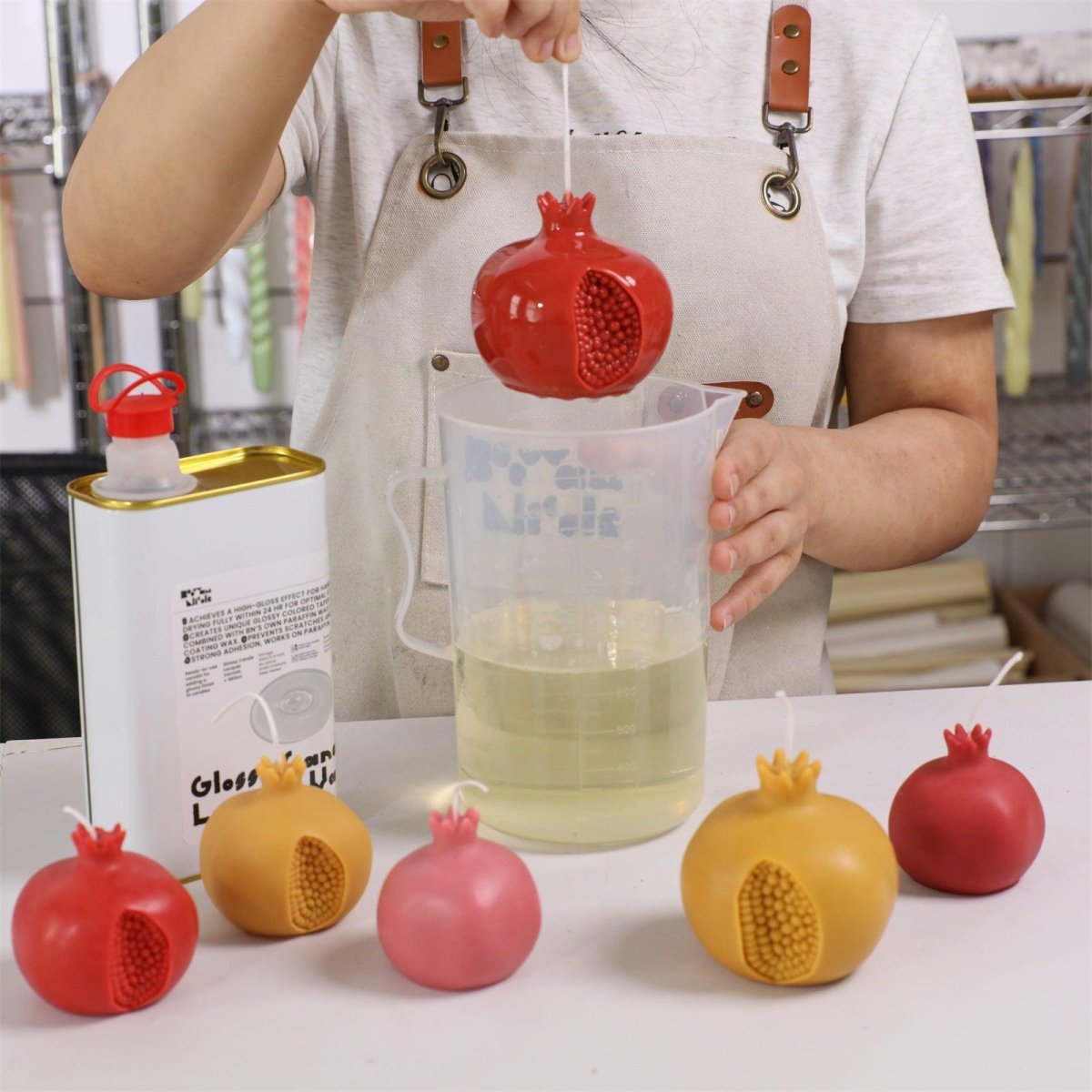 Dipping handcrafted pomegranate candles into glossy varnish—enhancing shine and sealing the surface for a polished finish - Boowan Nicole