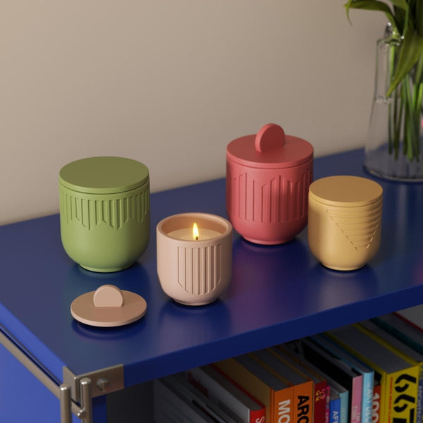 Colorful geometric candle jars with lids and one lit candle, styled on a blue shelf with books and decor - Boowan Nicole