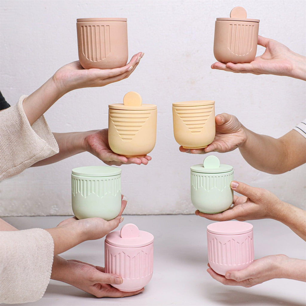 Hands holding pastel candle jars in beige, yellow, mint, and pink with geometric embossed designs - Boowan Nicole