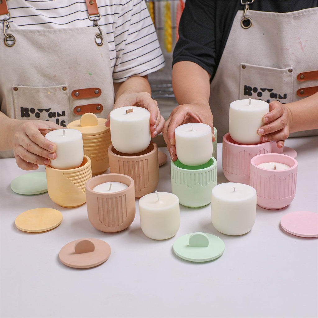 Two people assembling white candle refill into pastel geometric candle jars with matching lids on a table - Boowan Nicole