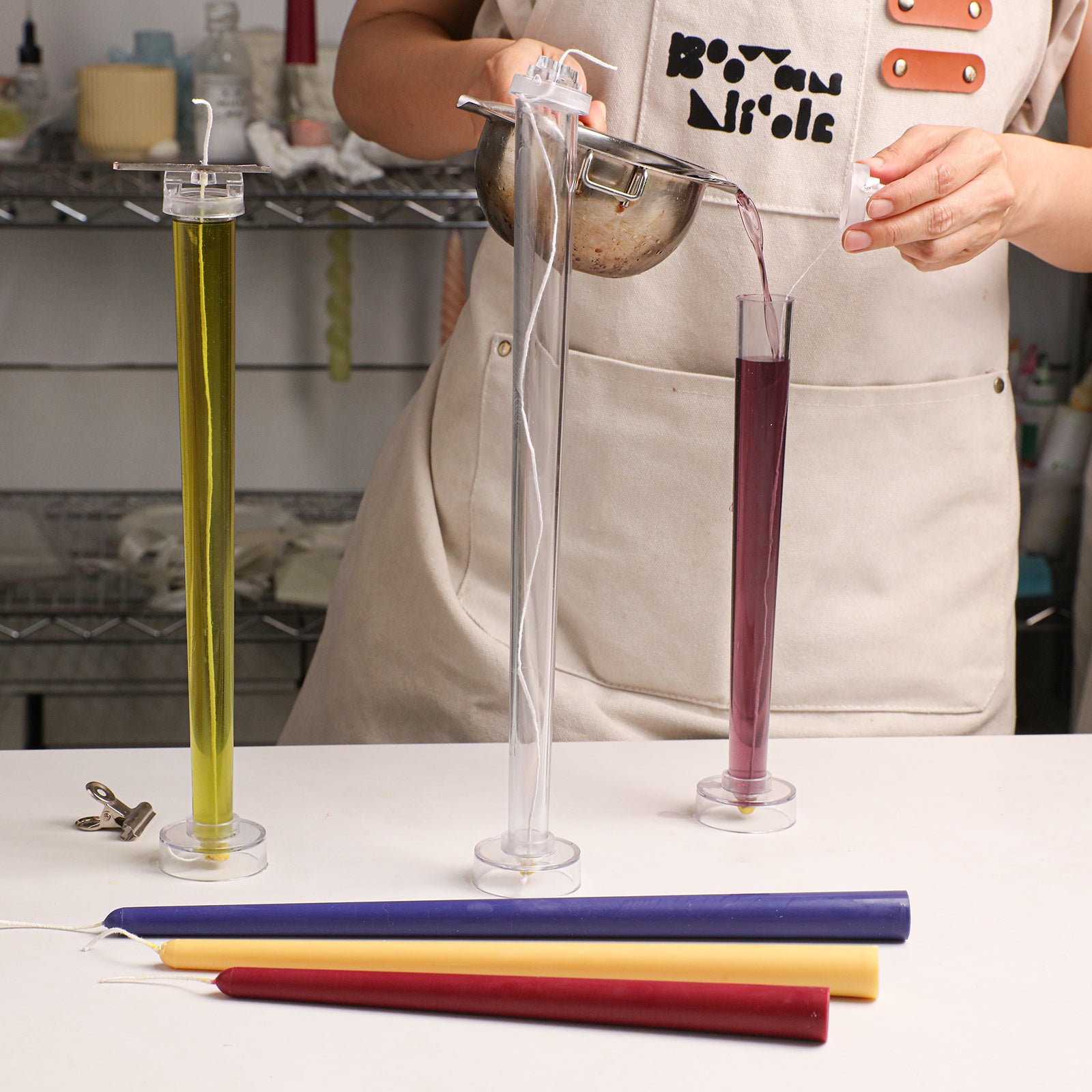 Round Top Taper Acrylic Candle Mold Collection, pouring melted wax into clear molds with Boowan Nicole branded apron - Boowan Nicole
