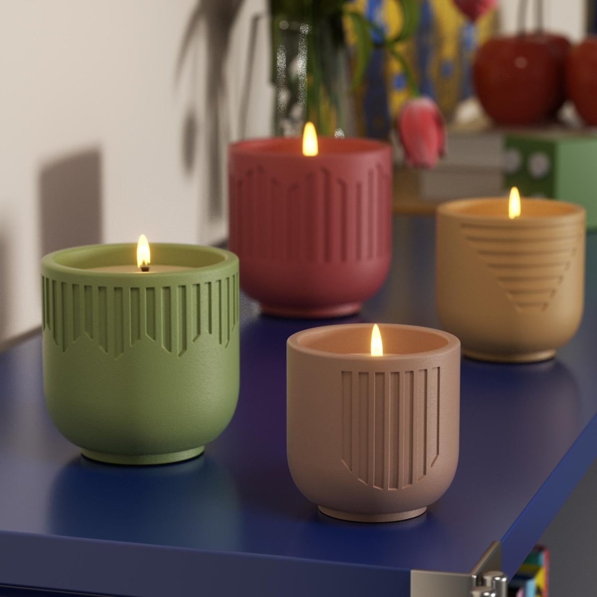 Lit candles in green, red, beige, and brown geometric jars on blue shelf - Boowan Nicole