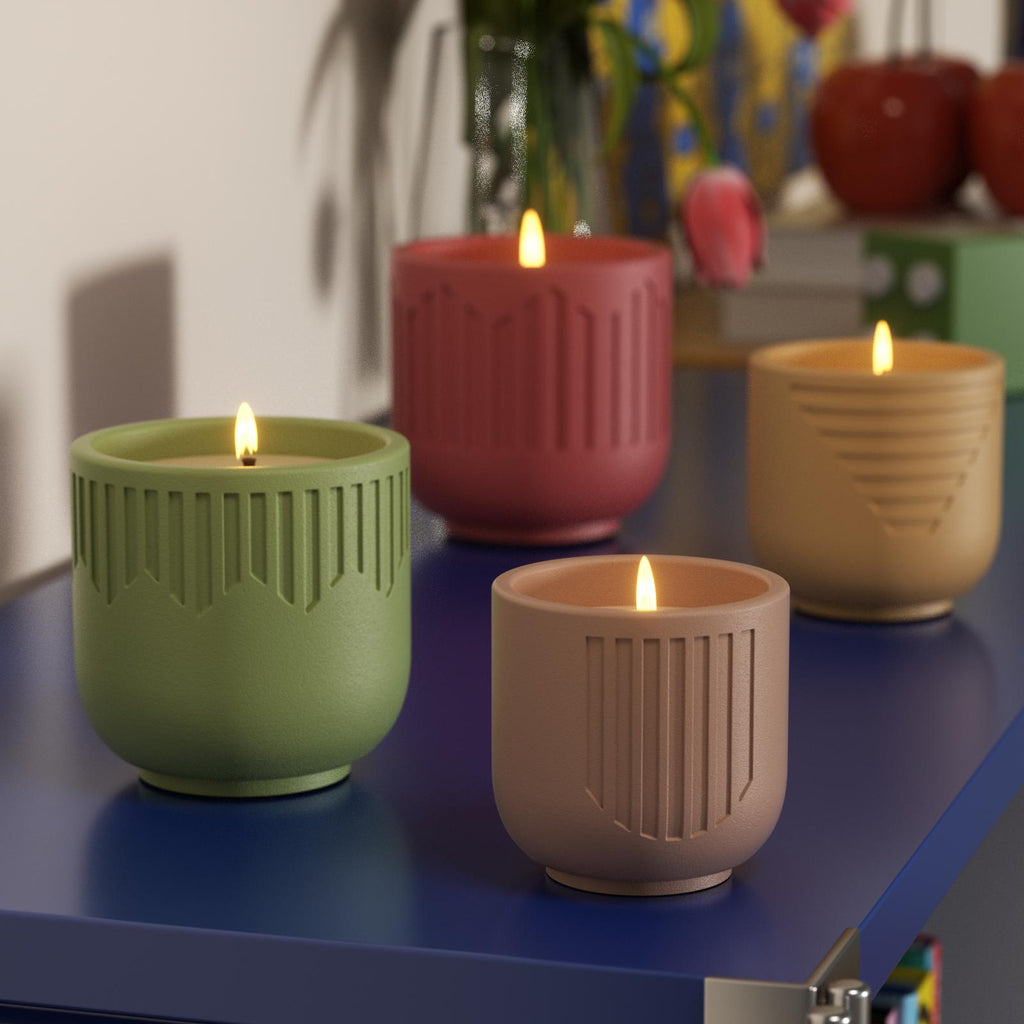 Lit candles in green, red, beige, and brown geometric jars on blue shelf - Boowan Nicole