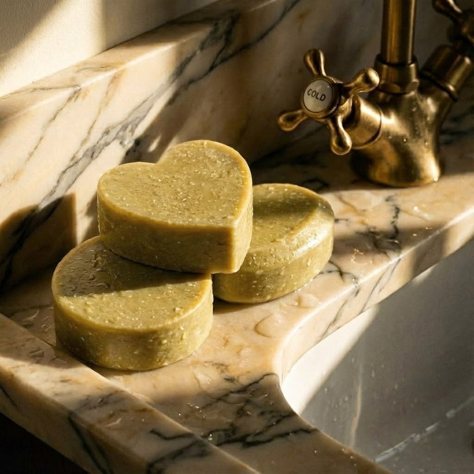 Three bars of green Herbal Sea Salt soap, including one heart-shaped bar, sitting on a luxury marble sink under warm natural sunlight - Boowan Nicole