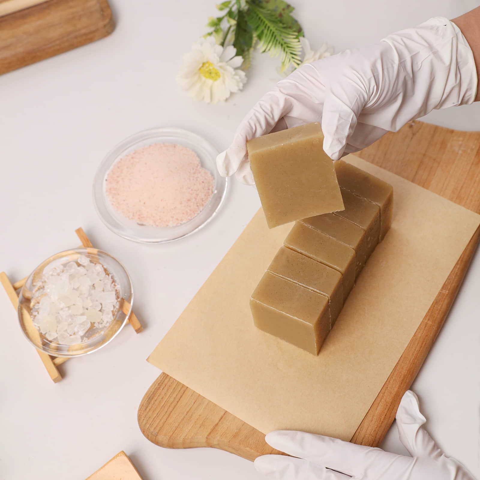 A gloved hand lifting a bar of Herbal Sea Salt Soap from a freshly cut block on a wooden board - Boowan Nicole
