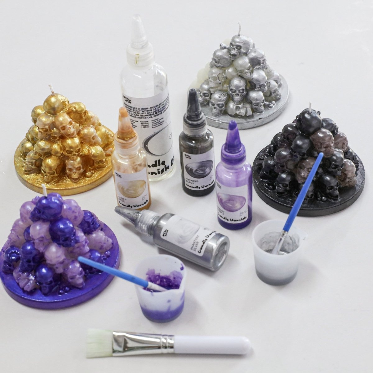 Hand-painted Skull Hill candles in metallic glossy varnishes—gold, silver, purple, and black—crafted with vivid Halloween-themed detail and DIY pigment tools - Boowan Nicole