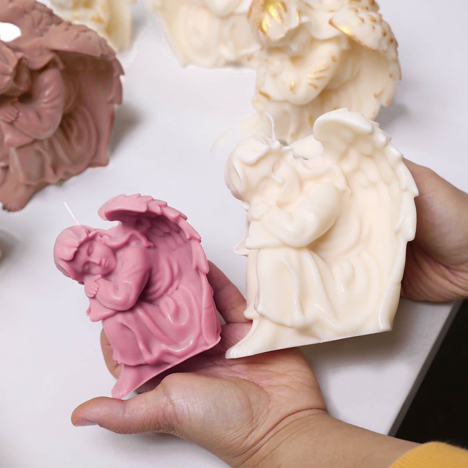 Hands holding small pink and large ivory sleeping angel pillar candles with folded wings - Boowan Nicole