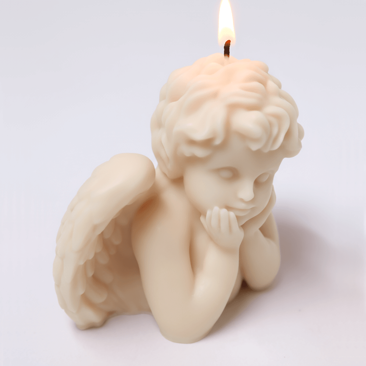 Sleeping Angel cherub pillar candle — ivory wax with folded wings, chin-in-hands pose, lit wick on a clean white background - Boowan Nicole