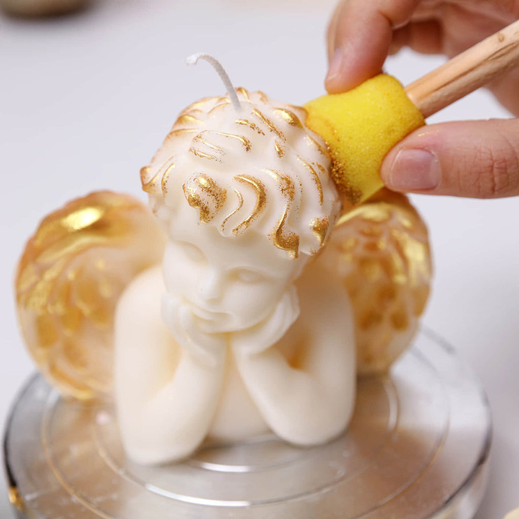 Hand-applying gold varnish to an ivory Sleeping Angel cherub candle with wings using a sponge dauber - Boowan Nicole