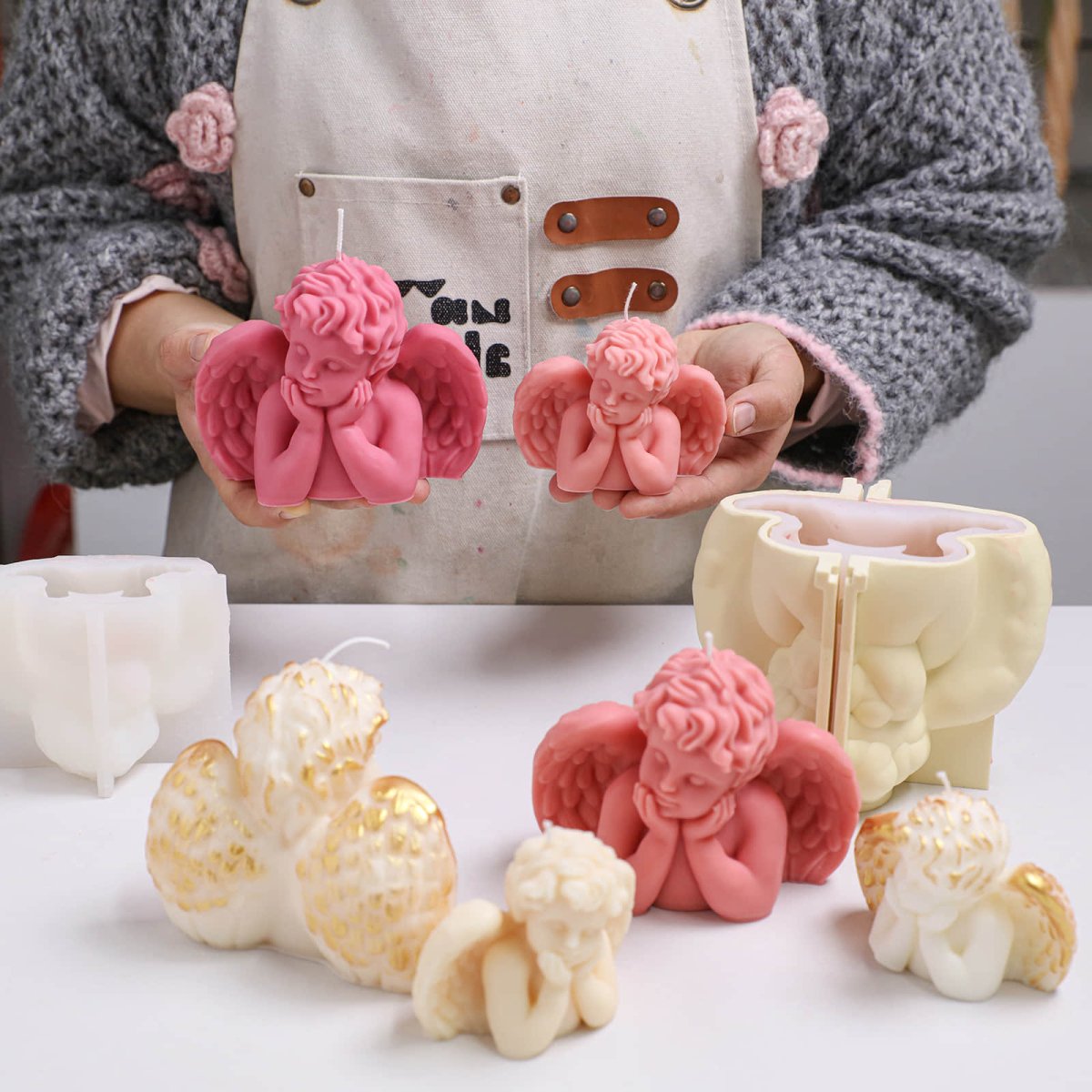 Maker holding large and small Sleeping Angel cherub candles; pink and ivory versions on table with support-shell silicone molds - Boowan Nicole