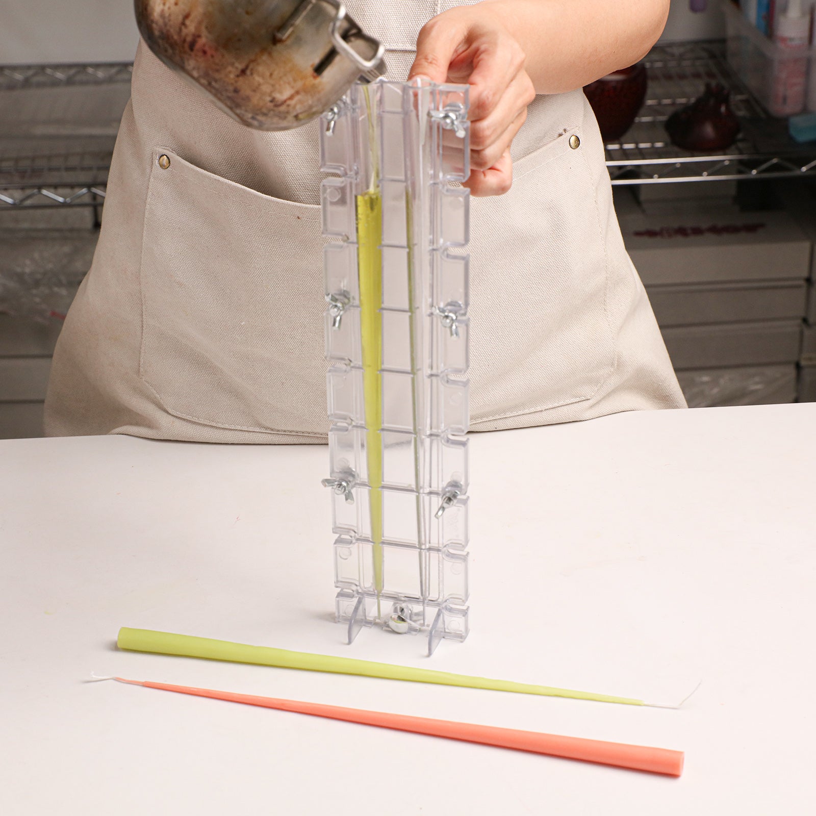 Ultra Slim Taper Acrylic Candle Mold, pouring melted wax into clear mold with finished slim taper candles - Boowan Nicole