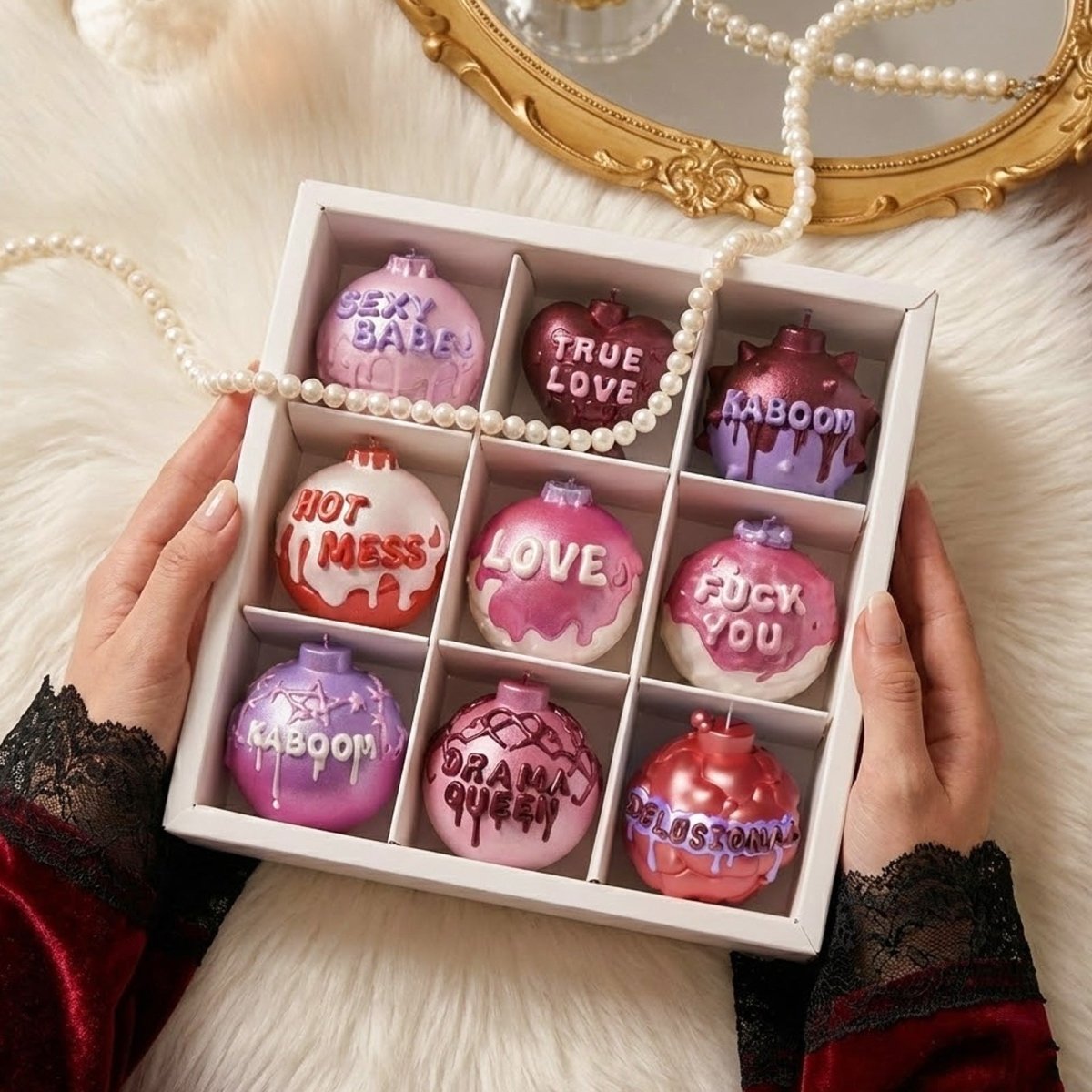 A white 9-compartment gift box containing shimmery Large Boomy Love sassy quote candles in various pink and purple hues - Boowan Nicole