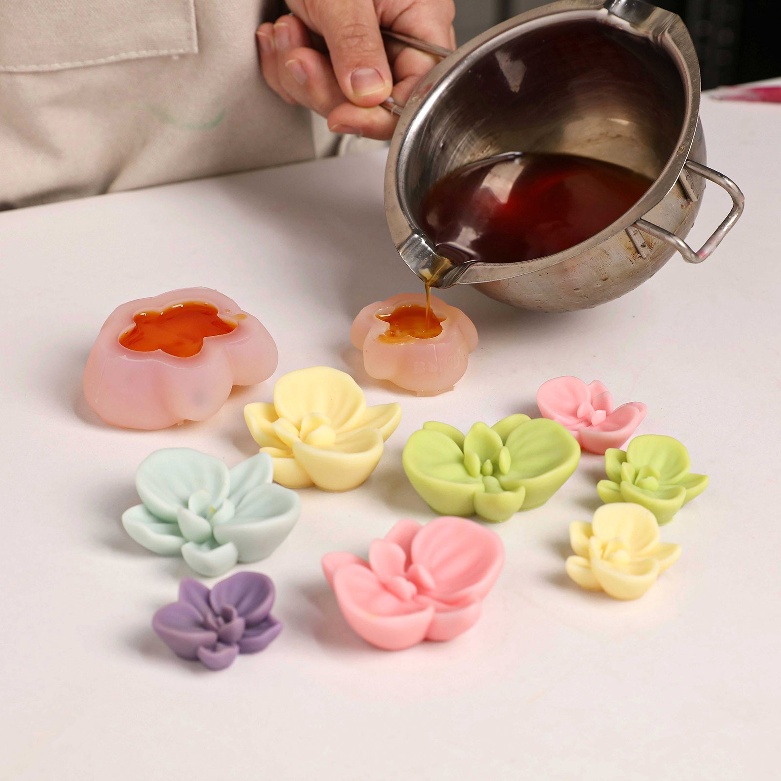 Pouring wax into silicone molds to create colorful orchid toppers, with finished pieces displayed. -Boowan Nicole