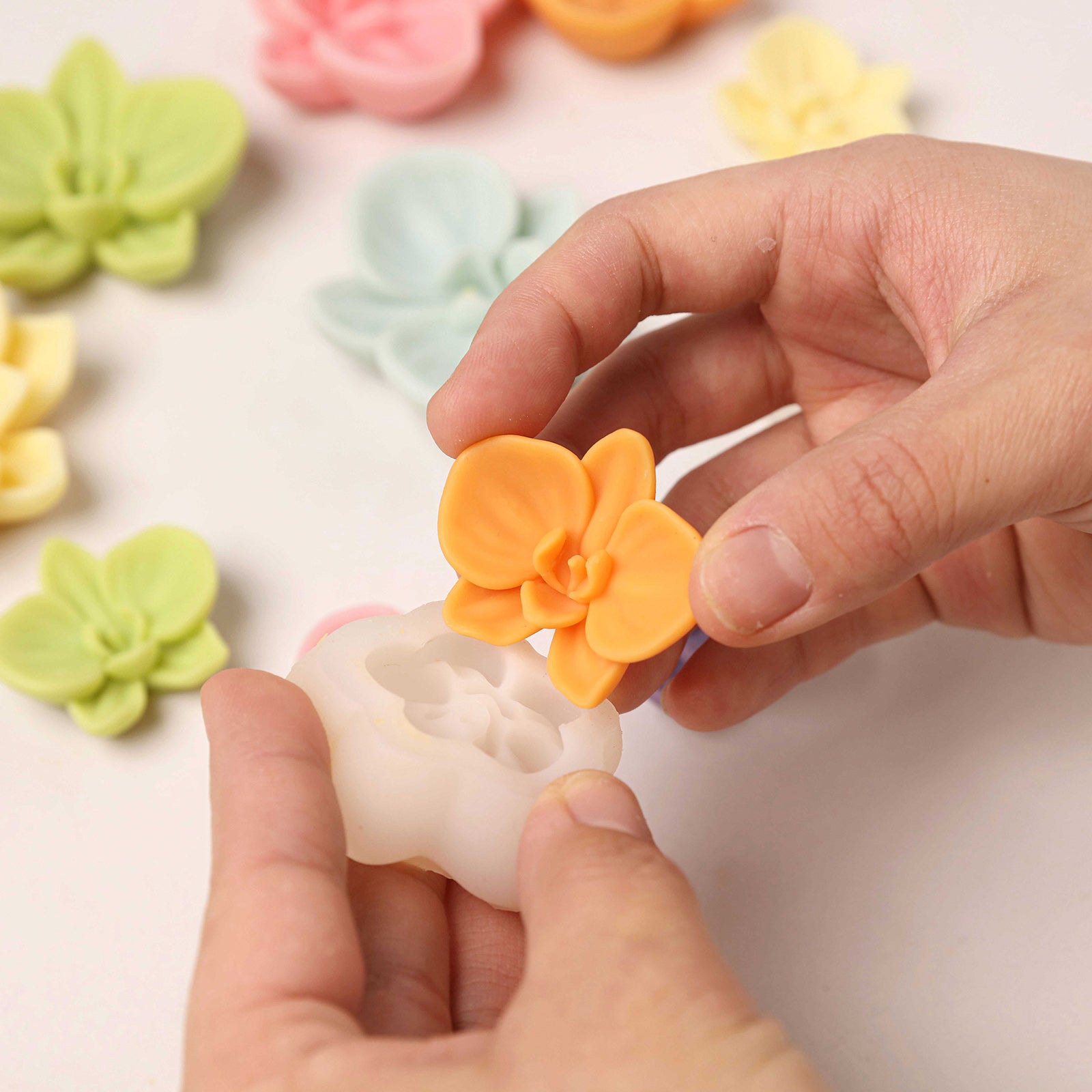 Demolding an orange orchid wax topper from a white silicone mold, showing easy release. -Boowan Nicole